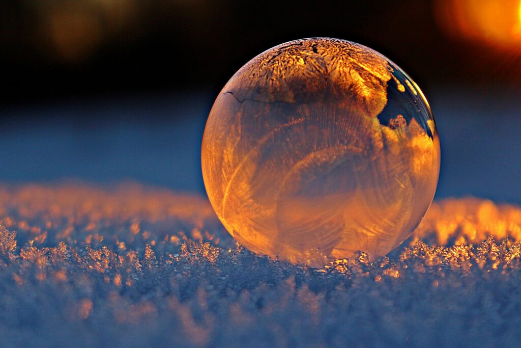 Close-up shot of a frozen bubble with warm reflections resting on a snowy surface at twilight.